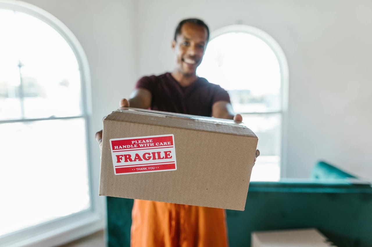 Hands holding a cardboard box labeled fragile, indicating careful handling during a move.